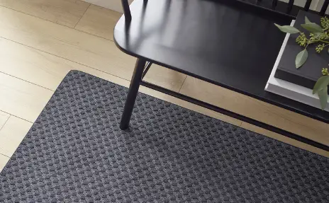 black textured area rug under black bench in hallway with light wood floors